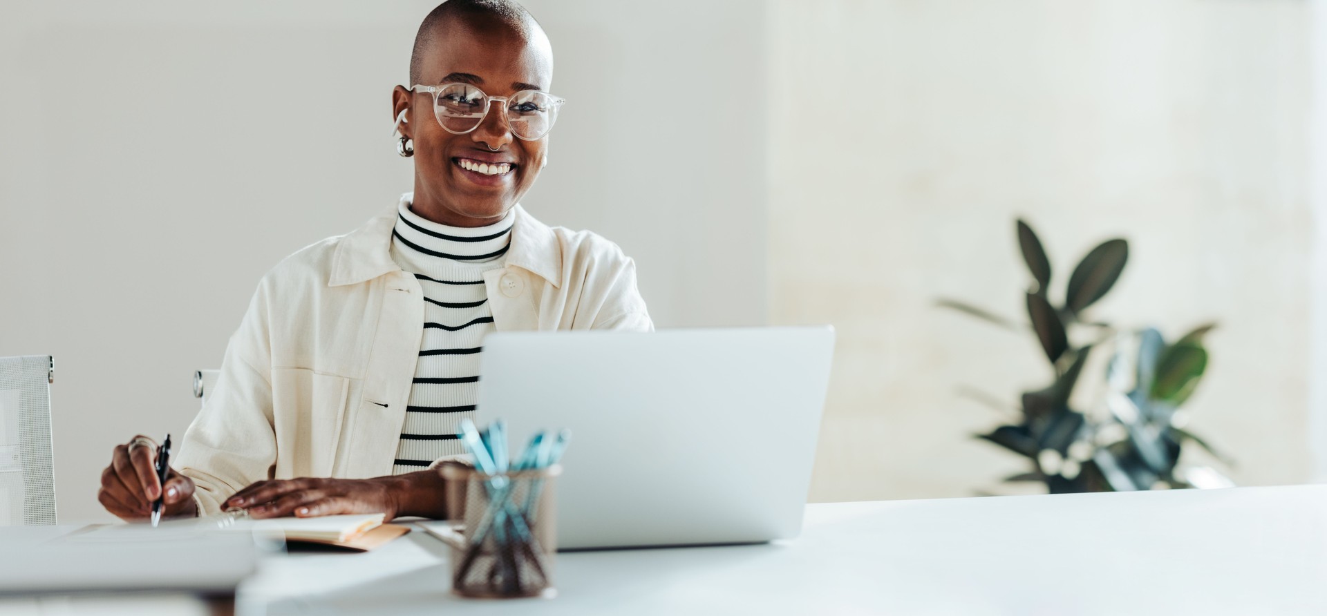 Portrait of a happy businesswoman working on a laptop in bright office with a notepad